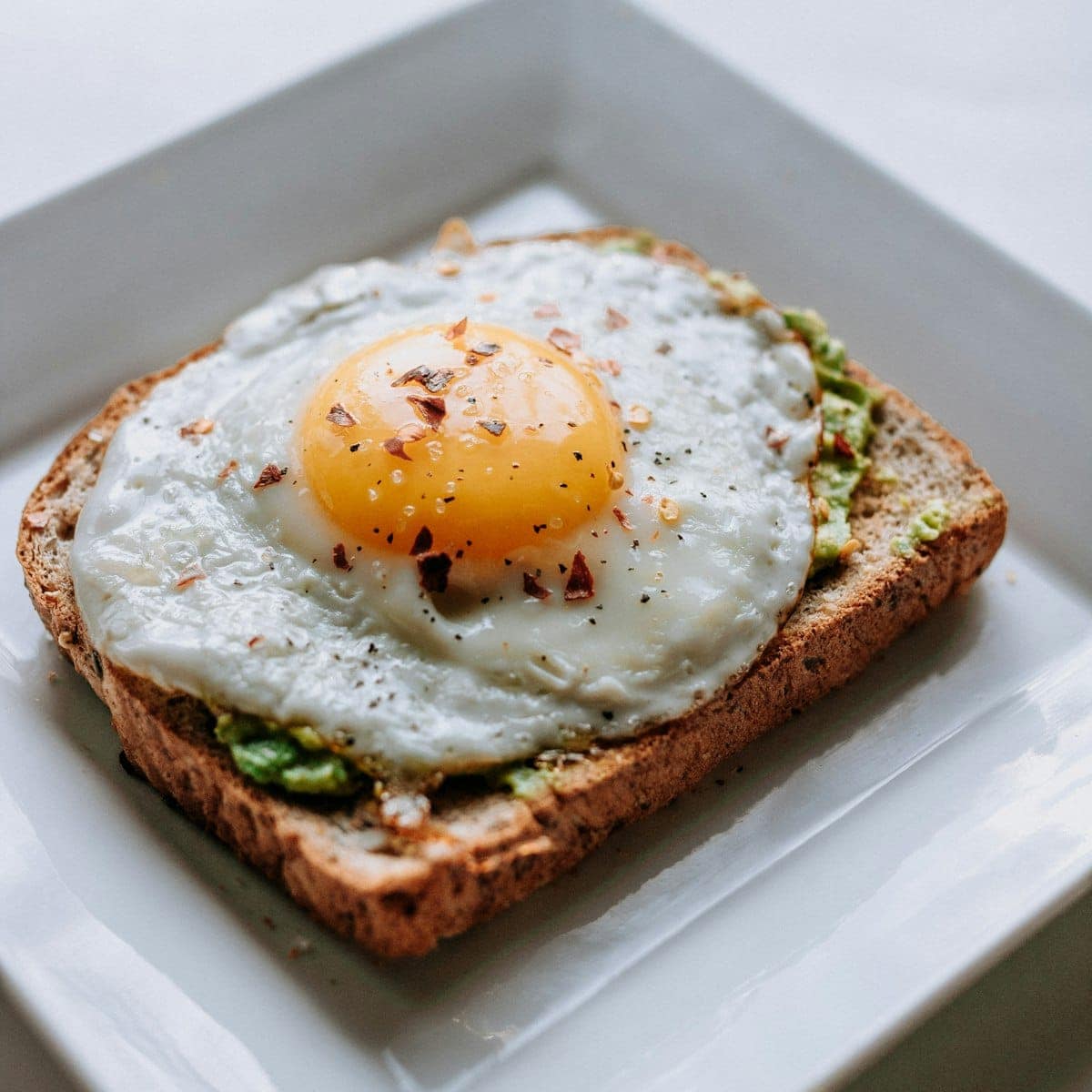 Halved soft-boiled jammy eggs with glowing liquid orange yolks sprinkled with flaky sea salt and cracked black pepper on a rustic board