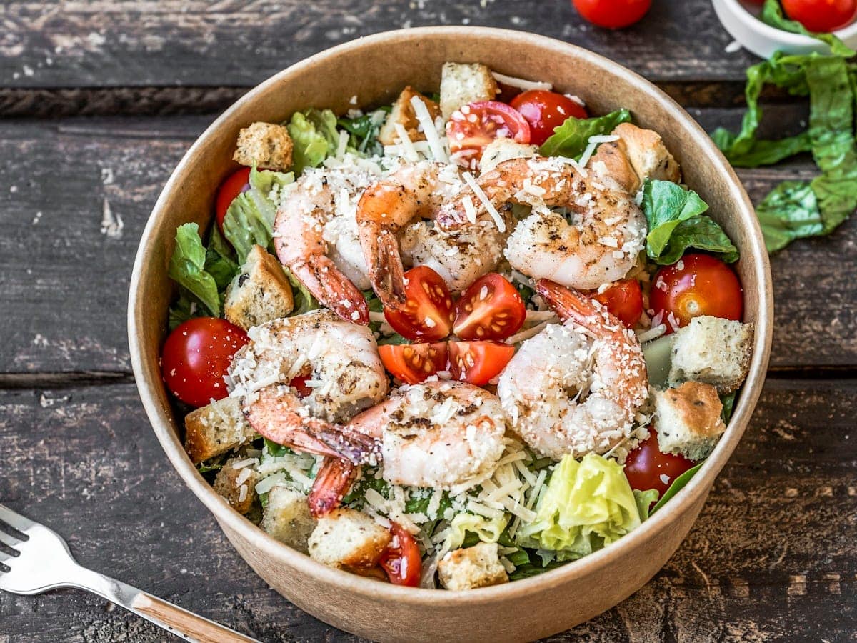 Plump golden brown pan seared jumbo shrimp tossed in garlic butter with freshly grated Parmesan cheese, herbs, and lemon in a wooden bowl