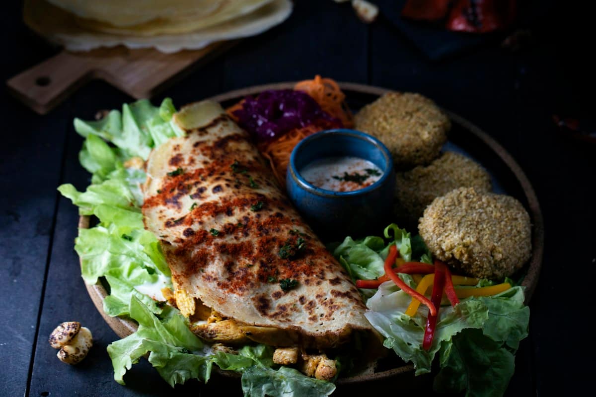 Warm flatbread wrap overflowing with tender, crispy charred chicken shawarma slices, creamy white garlic toum sauce, pickled wild cucumbers, and fresh parsley