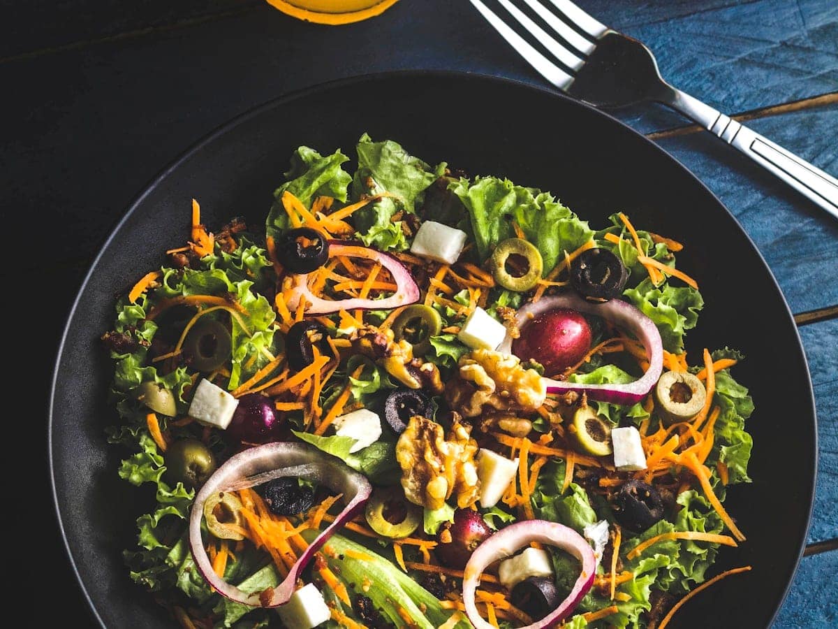 Vibrant Mediterranean chopped bistro salad in a black ceramic bowl with crisp curly greens, toasted walnuts, feta cheese cubes, olives, and red onion rings
