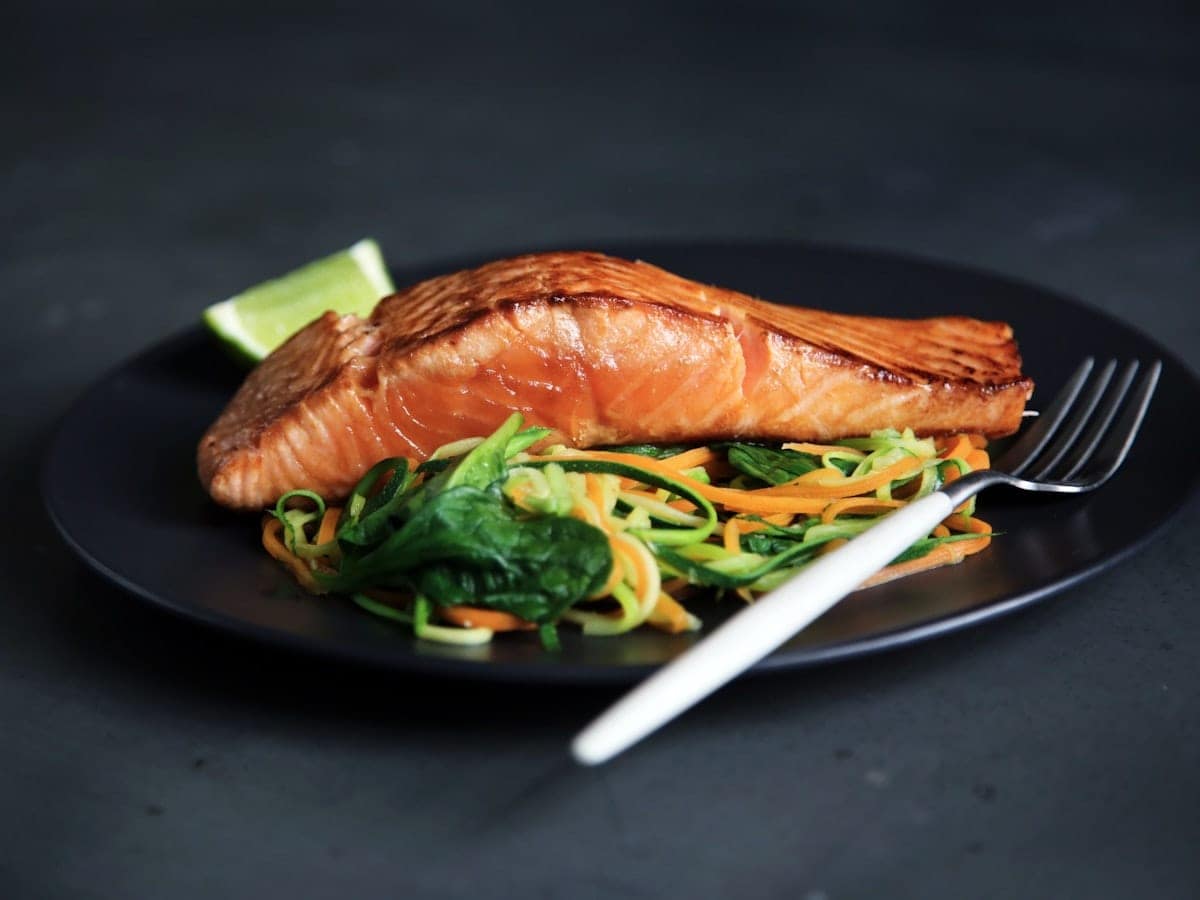 Pan-seared crispy skin salmon fillet in a glossy lemon caper butter pan sauce with fresh herbs and lemon slices
