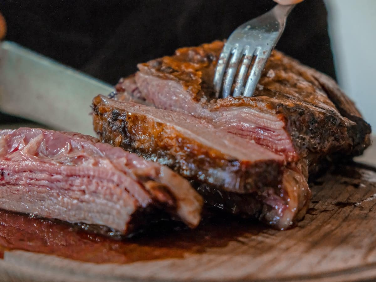 Juicy medium rare pan seared ribeye steak carved into thick tender slices showing golden brown caramelized crust on a rustic cutting board