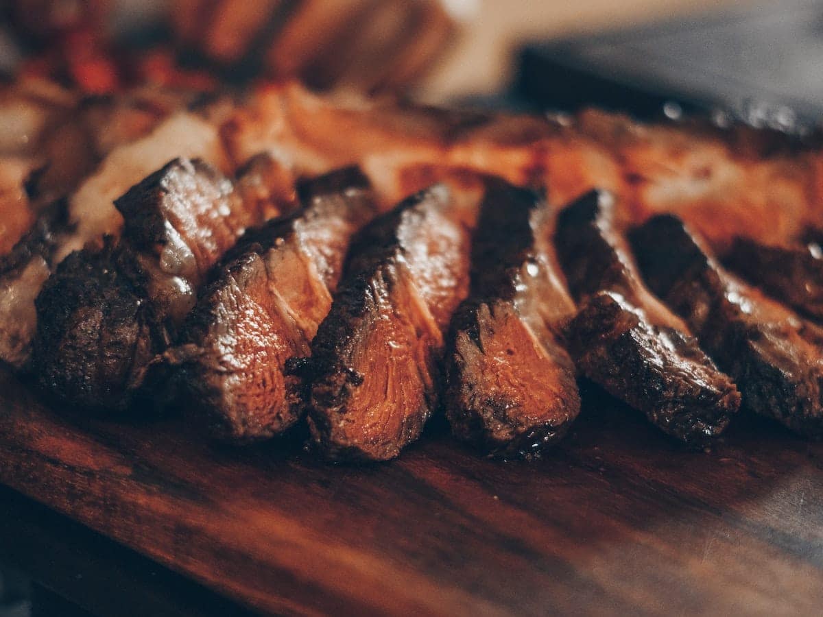Thick sliced pan-seared juicy lamb steaks with a caramelized herb crust and pink tender center carved on a dark wooden cutting board