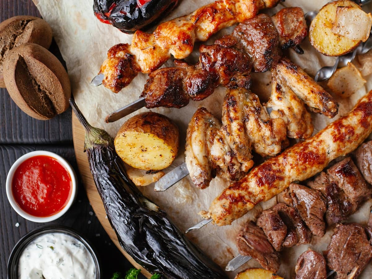 Sizzling charred Mediterranean spiced lamb kebabs on skewers served with roasted vegetables, flatbread, and cool garlic herb yogurt sauce