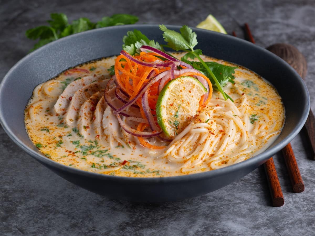 Rich golden yellow creamy coconut chickpea curry in a ceramic bowl with herbs and lime