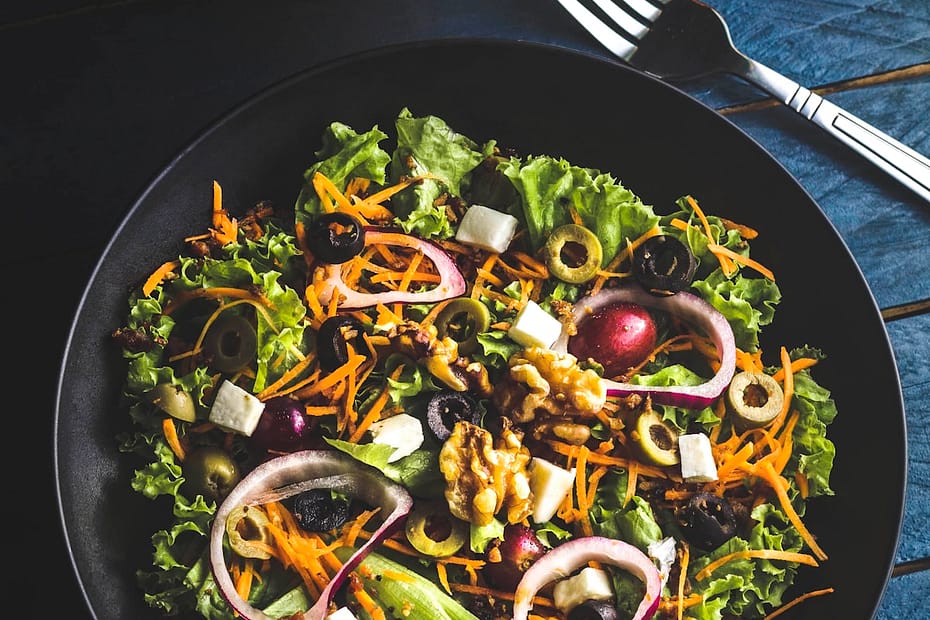 Vibrant Mediterranean chopped bistro salad in a black ceramic bowl with crisp curly greens, toasted walnuts, feta cheese cubes, olives, and red onion rings