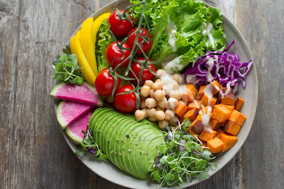 Vibrant ceramic bowl filled with fan-sliced avocado, sweet potato cubes, chickpeas, cherry tomatoes, watermelon radish, and creamy lemon tahini dressing