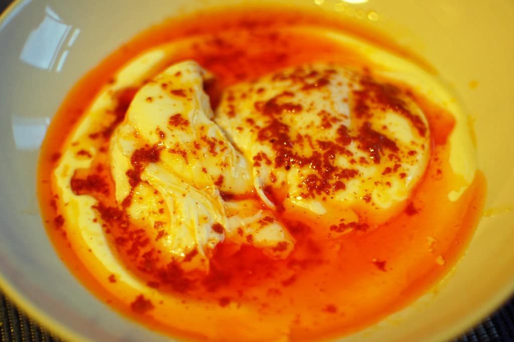 Authentic Turkish eggs cilbir in a shallow white ceramic bowl with whipped garlic yogurt and foaming red Aleppo chili butter